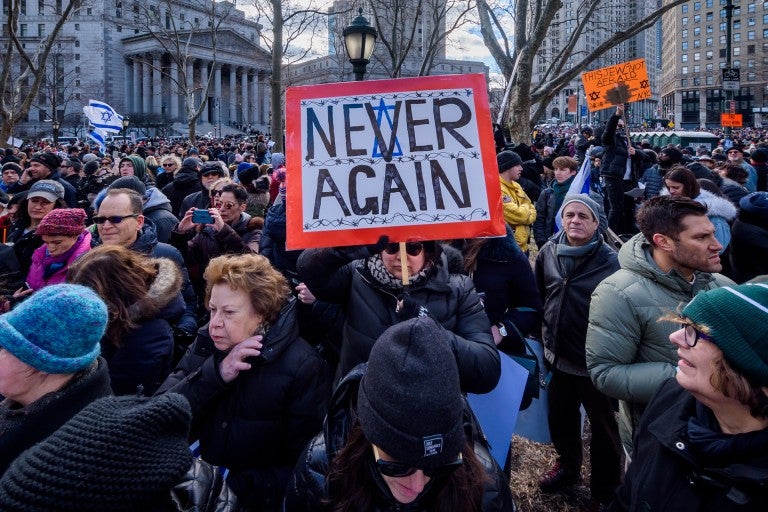 Photo of a crowd and a woman holding a sign saying "Never Again"