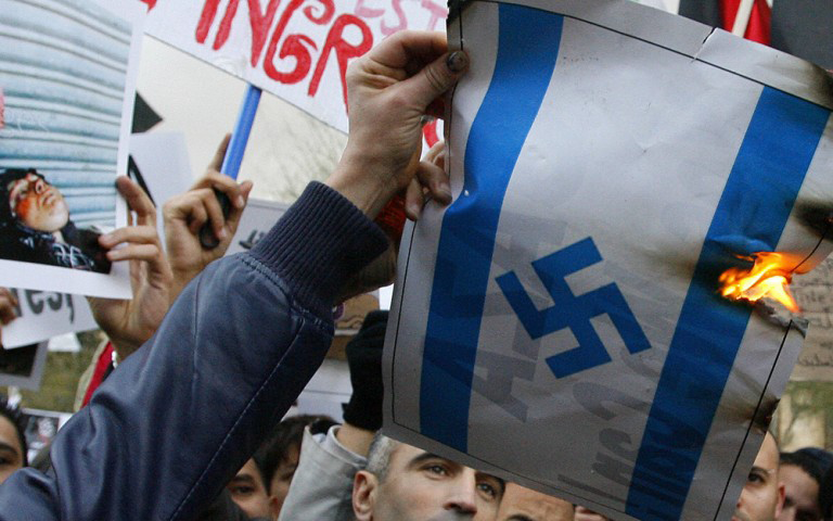 Photo of a man burning a picture of an Israeli flag with a swastika 