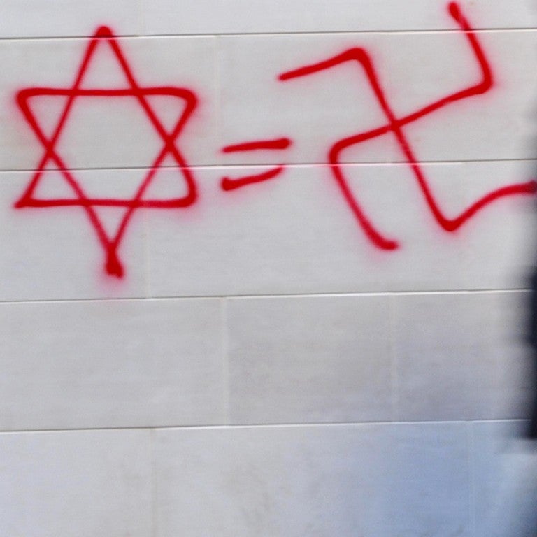 Photo of a Star of David, an equal sign, and a Swastika graffitied on a wall