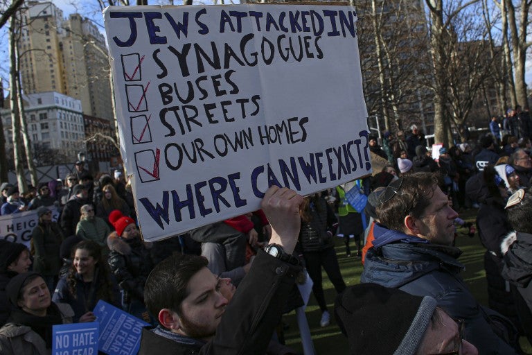 Man holding a sign "Jews attacked in synagogues, buses, streets and our home. Where can we exist?"