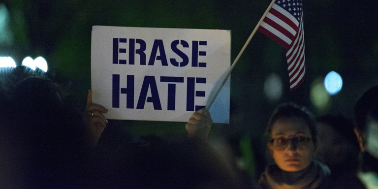 Women holding a sign saying "Erase Hate"