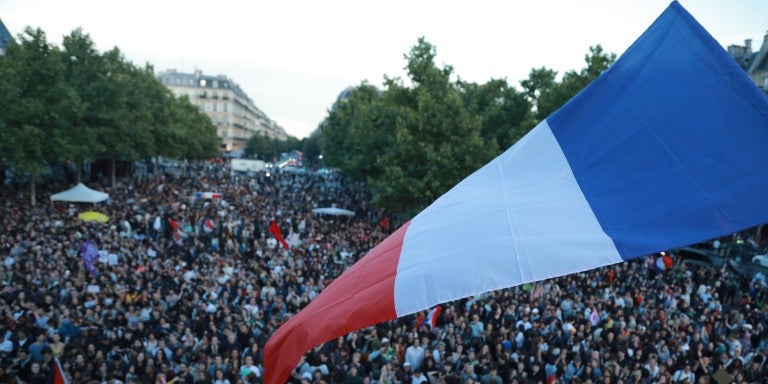 Large french flag waving outside in front of a crowd post-French elections in July 2024