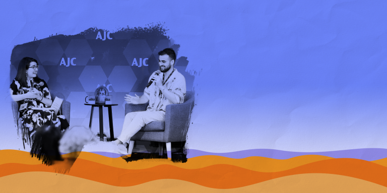 Photo of Adiel Cohen and Manya Brachear Pashman, both smiling and sitting in armchairs with a small endtable in the middle, on a stage in front of a step and repeat with AJC lettering, paintbrush effect around the photo, laid over a graphic representation of the desert