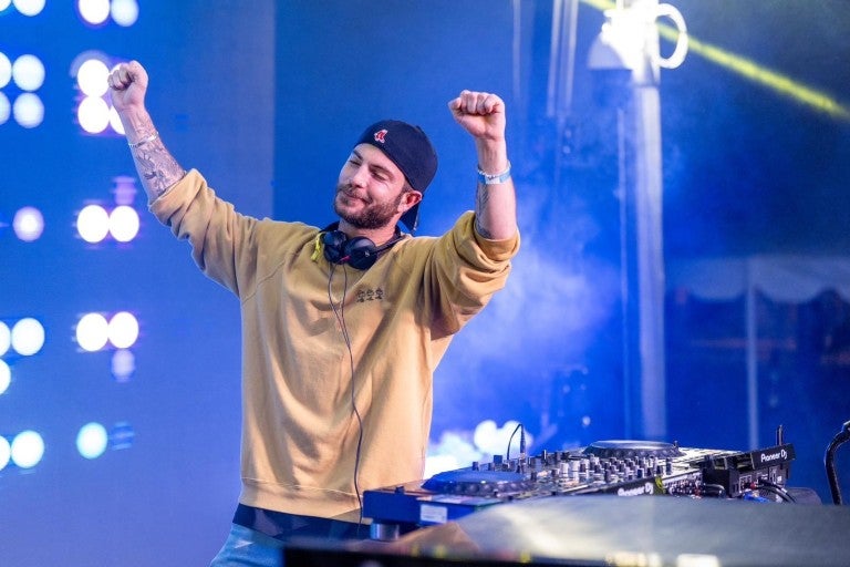 Israeli DJ Daniel Vaknin, in a yellow sweater stands with his arms raised, expressing joy or celebration. 