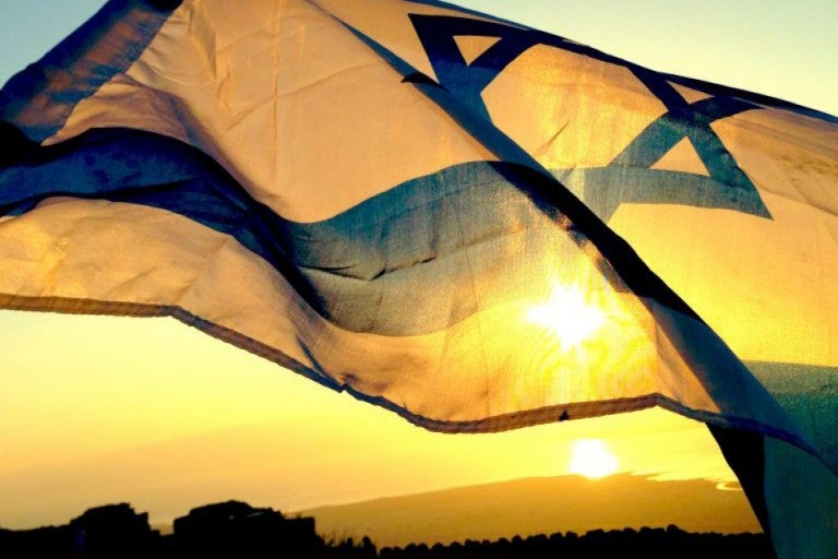 Photo of Israeli flag waving with a sunset in the background