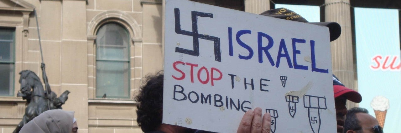 Photo of a protest sign with a Swastika saying "Israel stop the bombing"
