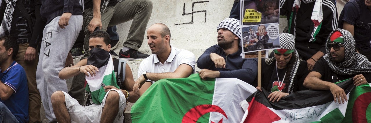 A group of extremist Muslims in Europe gathers around a statue with a swastika graffitted on it 