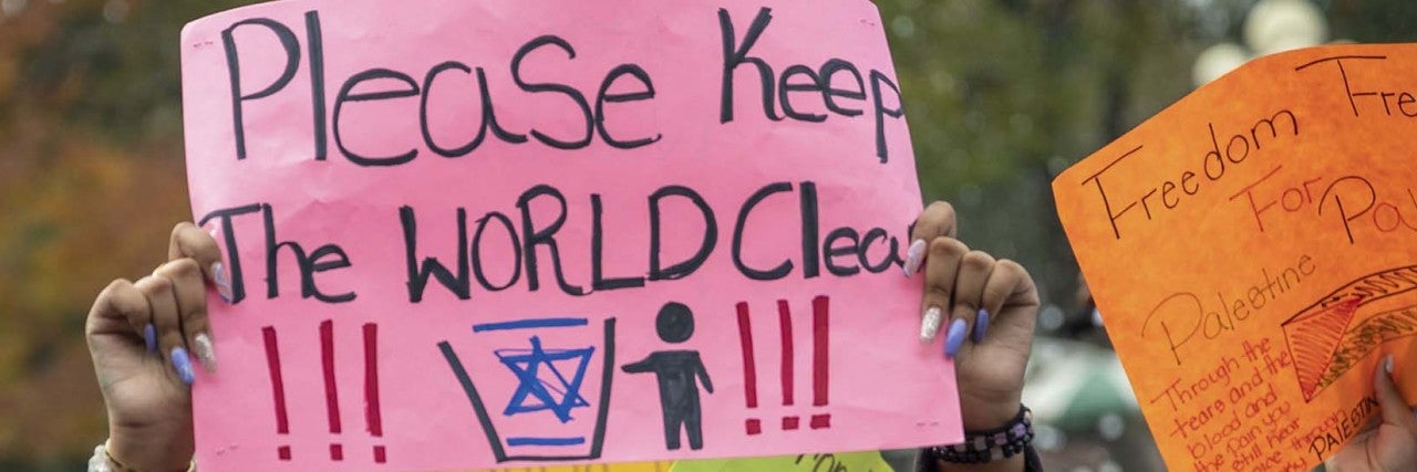 Sign at protest - "Please keep the world clean" with a photo of a person throwing away the Jewish star