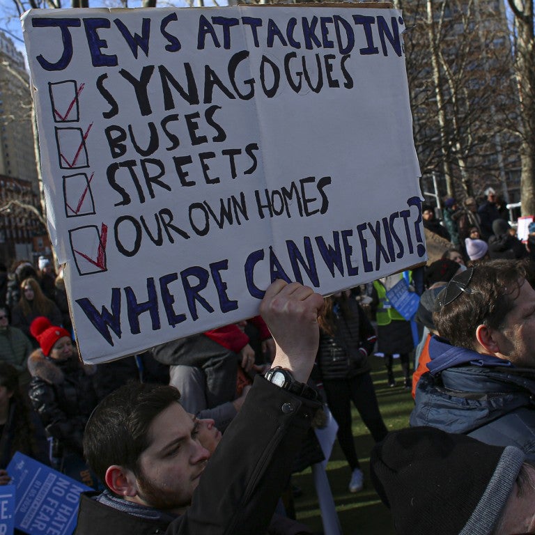 Man holding a sign "Jews attacked in synagogues, buses, streets and our home. Where can we exist?"
