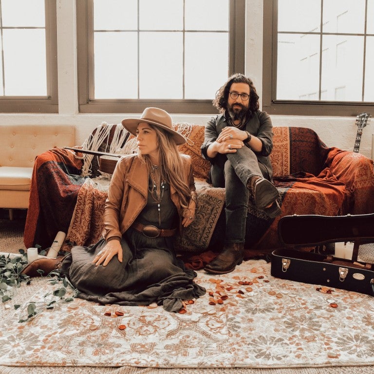 woman sitting on the floor, man sitting on a couch behind her, of the jewish bluegrass band nefesh mountain