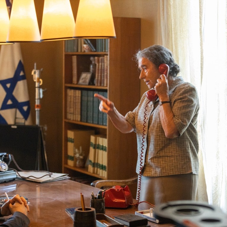 Helen Mirren standing in front of a desk, on the phone, pointing a finger, in her role as Golda Meir in Bleecker Street/ShivHans Pictures -GOLDA. Credit: Sean Gleason, Courtesy of Bleecker Street/ShivHans Pictures