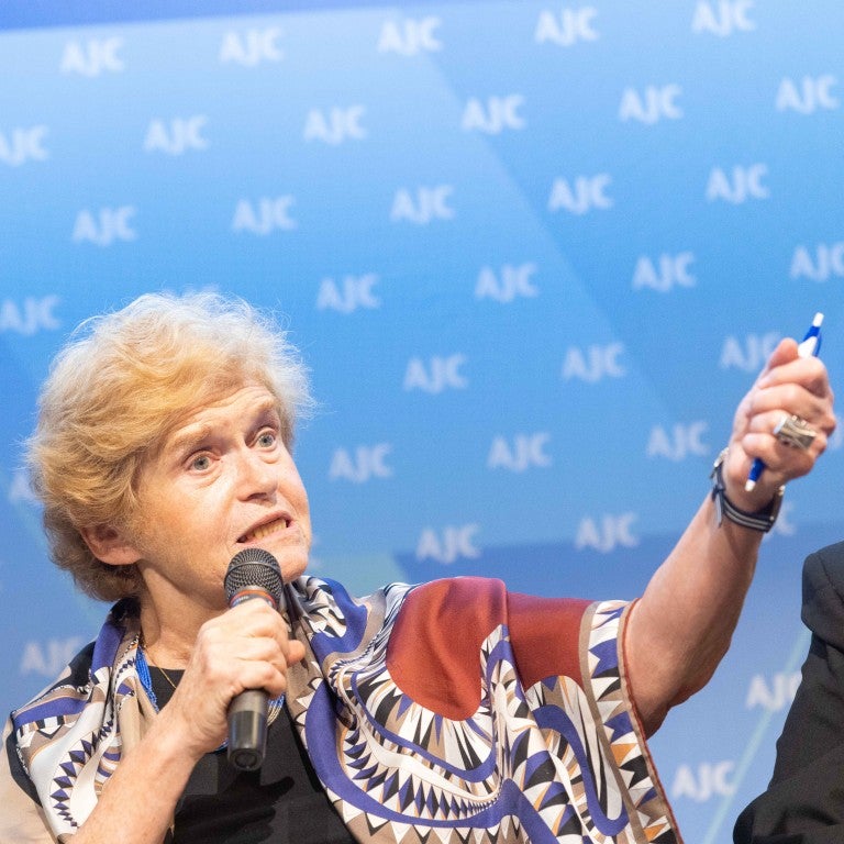 deborah lipstadt in front of blue AJC step and repeat. wearing a reddish shawl, and a jewish star magen david necklace