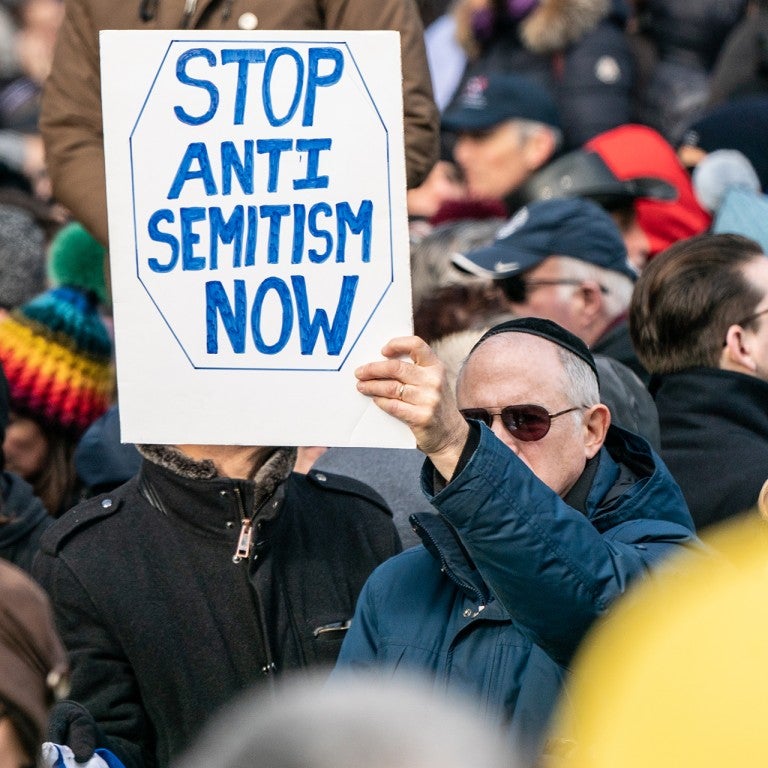 Photo of man holding a sign saying Stop Antisemitism Now