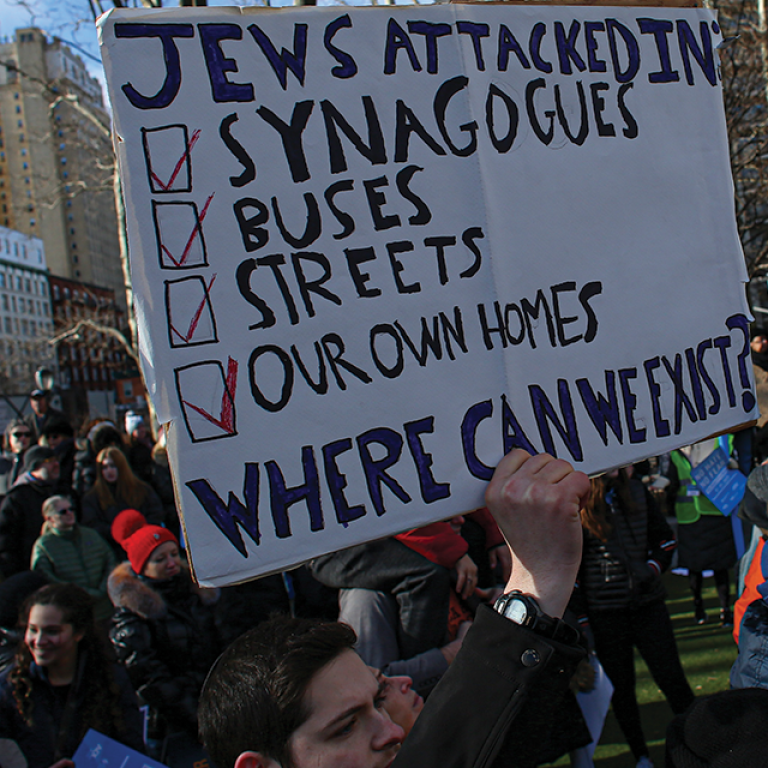Photo of a man holding up a sign saying "Jews attacked in Synagogues, Buses, Streets, Our Own Homes where can we exist?"